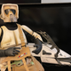 A 12-inch Star Wars Scout Trooper toy poses heroically next to his speeder bike.